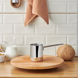 Emsan Aaron 500 ml stainless steel cezve pot on wooden board with milk, coconut, and kitchen towel in modern kitchen