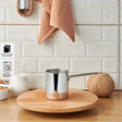 Emsan stainless steel Turkish coffee pot on wooden board with coconut, milk jug, and hanging towel
