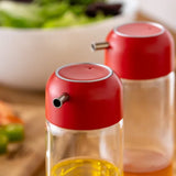 Close-up of red-topped glass oil and vinegar dispensers with spouts on wooden countertop