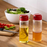 Emsan Jordan glass oil and vinegar dispensers with red caps on wooden kitchen countertop with salad bowl and chopped vegetables